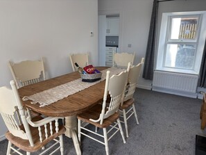 Comedor con mesa de madera y sillas blancas, un tapete y una cesta de aperitivos.
