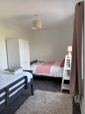 A bedroom with two beds, a wardrobe, a bedside table, a lamp, and a window with curtains.