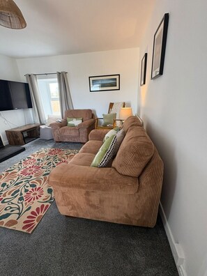 Ein Wohnzimmer mit Sofa, Sessel und einem an der Wand befestigten Flachbildfernseher.