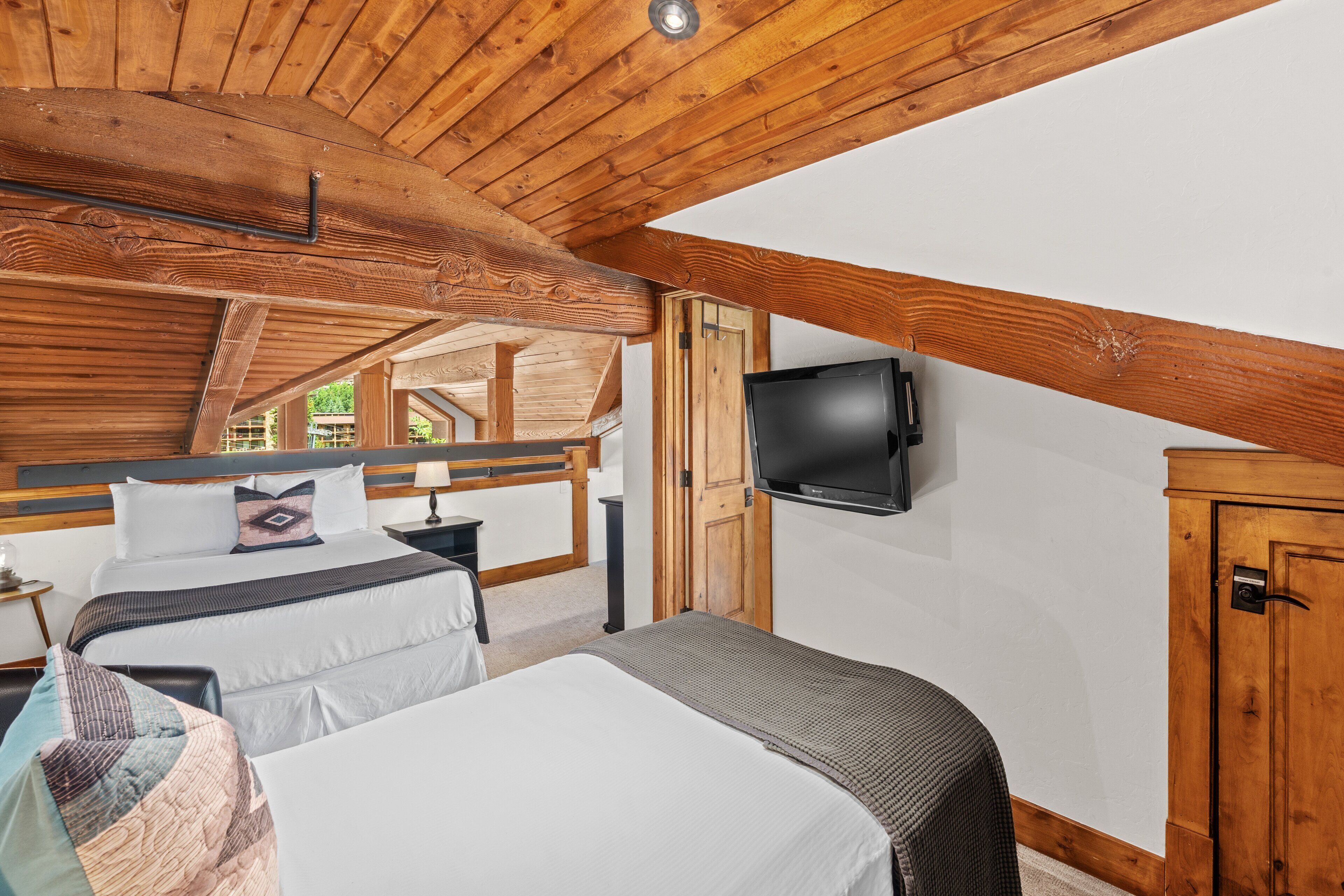 Une chambre avec un plafond en bois, un téléviseur fixé au mur et un lit recouvert d’une courtepointe matelassée.