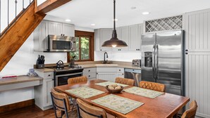Una cocina con piso de madera, una mesa de comedor con cuatro sillas, un refrigerador de acero inoxidable y un microondas.