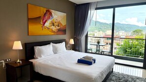 A hotel room with a large bed, two bedside lamps, a painting, and a balcony with a city view. - Emerald 307 - Studio With Balcony and Shared Pool (Patong)