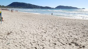 En sandstrand med fotspår, en livräddarstation och en fri utsikt över havet och de avlägsna kullarna.