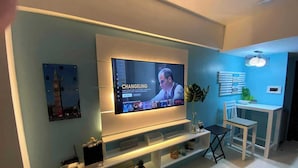 A modern living room with a flat-screen TV mounted on the wall, a small table with a chair, and a decorative plant. - One Palm Tree Villas near NAIA 3 (Pasay)