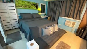 A bedroom with a bed, a dresser, a nightstand, a window with curtains, and a wall-mounted air conditioning unit. - One Palm Tree Villas near NAIA 3 (Pasay)