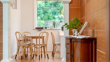 A dining area with a table and chairs, a window with a view of greenery, and a cabinet with a plant.