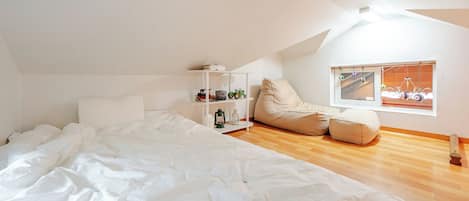 Una camera da letto con un letto grande, una finestra vista sulle biciclette, uno scaffale con dei giocattoli e un pouf.