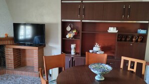 A dining area with a brick fireplace, a television mounted above it, and wooden cabinets above the cabinets.