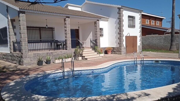 A residential property with a swimming pool, stone pillars, and a covered patio area.
