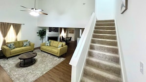 A spacious living room with a high ceiling, a staircase, and a fireplace.