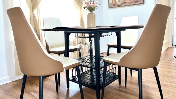 A dining area with a table and four chairs, a vase with flowers, and a painting on the wall.