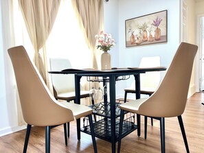 Un comedor con una mesa y cuatro sillas, un jarrón con flores y un cuadro en la pared.