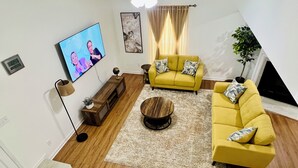 A living room with a yellow sofa, a coffee table, a TV, and a plant.
