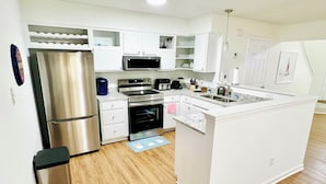 A modern kitchen with white cabinetry, stainless steel appliances, and a wooden floor.