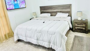 A bedroom with a bed, a TV mounted on the wall, a nightstand, a lamp, and a framed picture of giraffes.