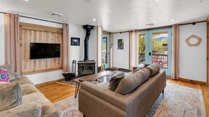 Una sala de estar con sofá, televisor, chimenea y vistas a través de un ventanal.