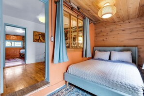 A bedroom with a wooden ceiling, a bed with white bedding, and a window with curtains.