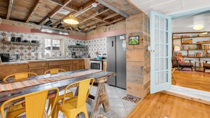 Una cocina con armarios de madera, una mesa de comedor con sillas amarillas, un refrigerador y una estantería.