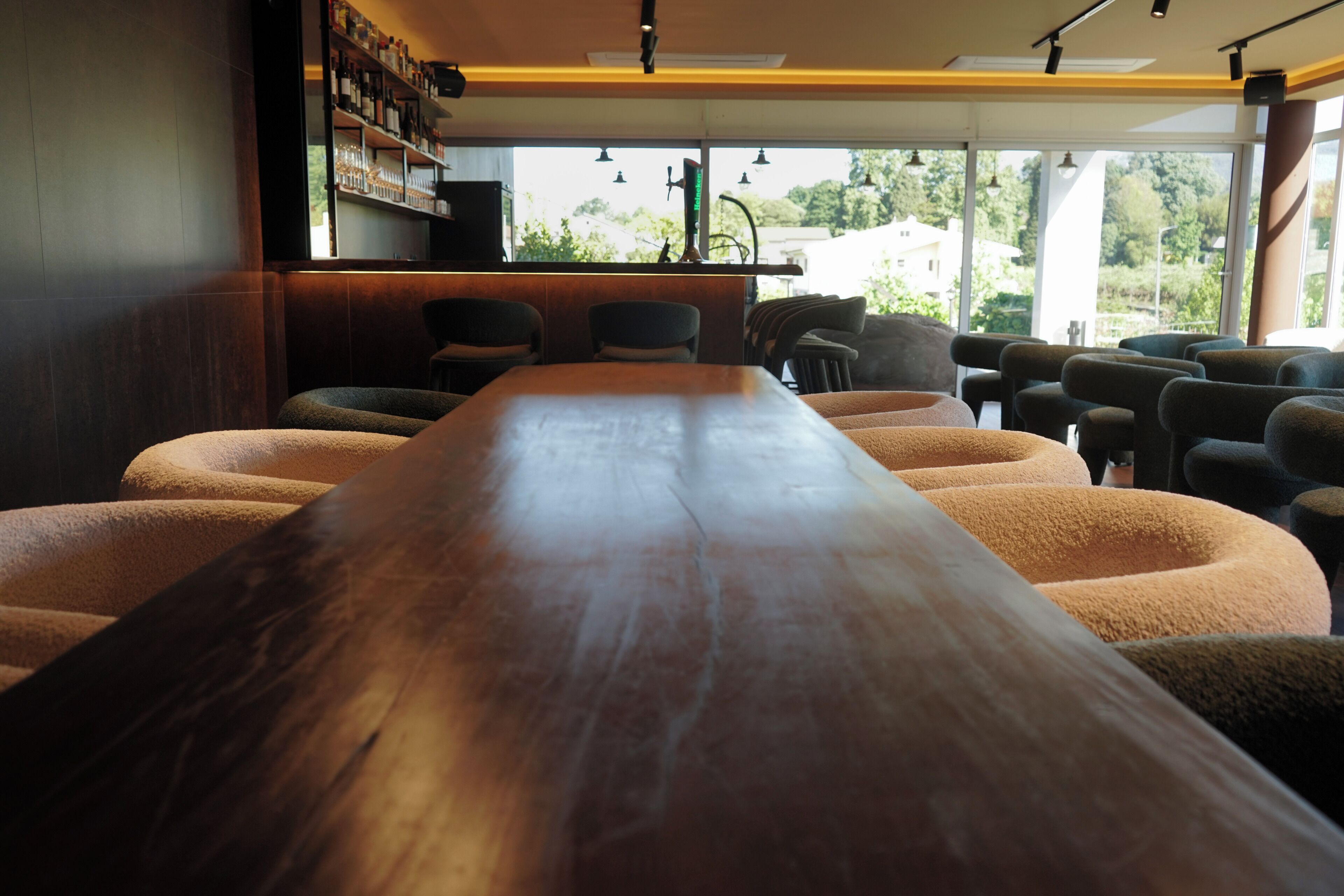 Een lange houten tafel met stoelen, een bar met planken, en grote ramen met uitzicht.