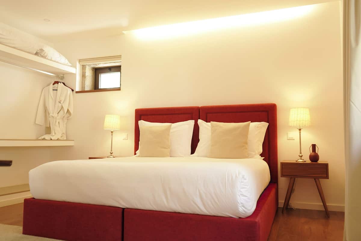 A hotel room with a large bed, two bedside tables, a nightstand, a robe hanging on a rack, and a window with a view.