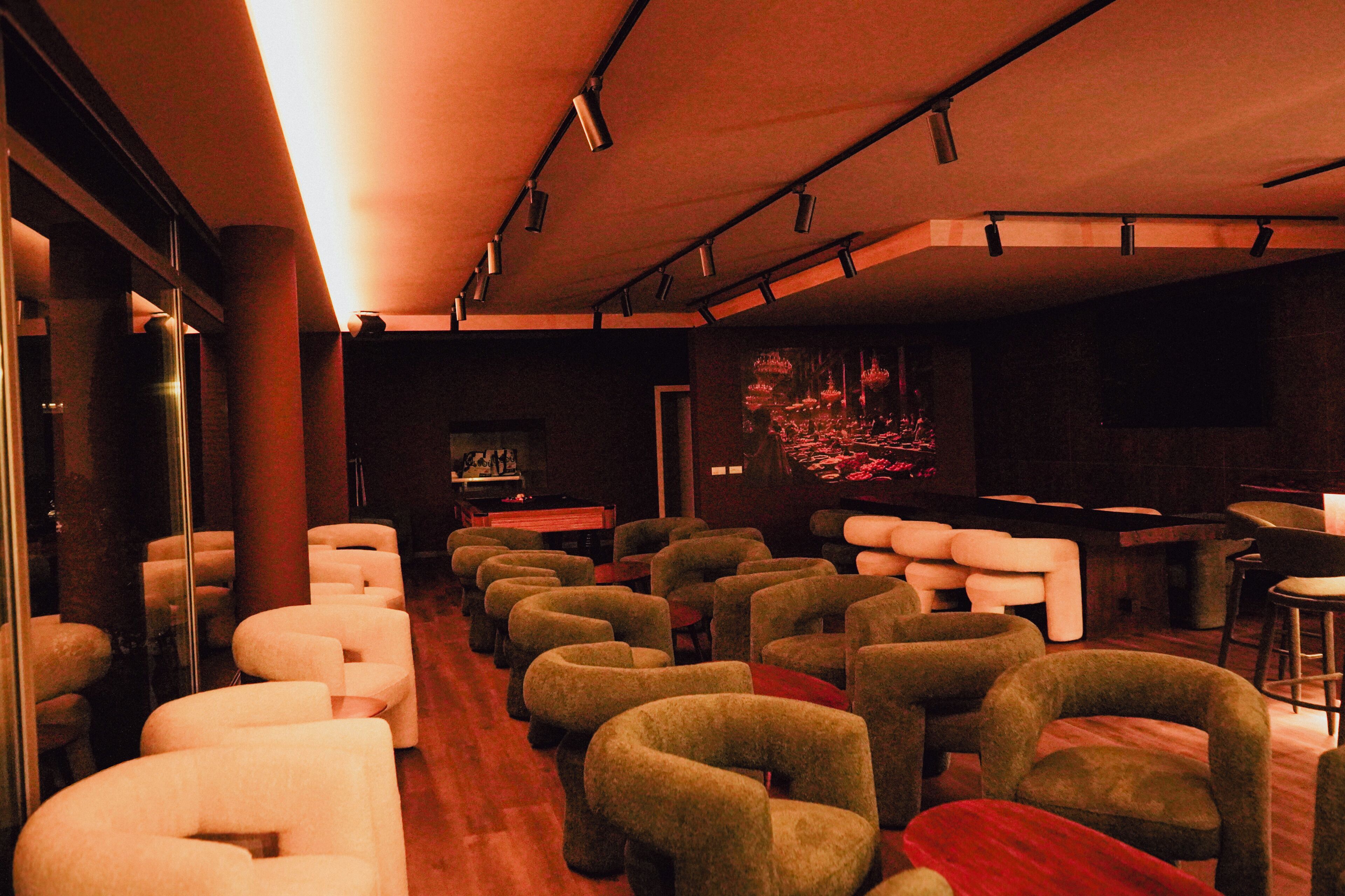 Un hall d’hôtel avec plusieurs rangées de sièges, un espace bar et un écran fixé au mur.