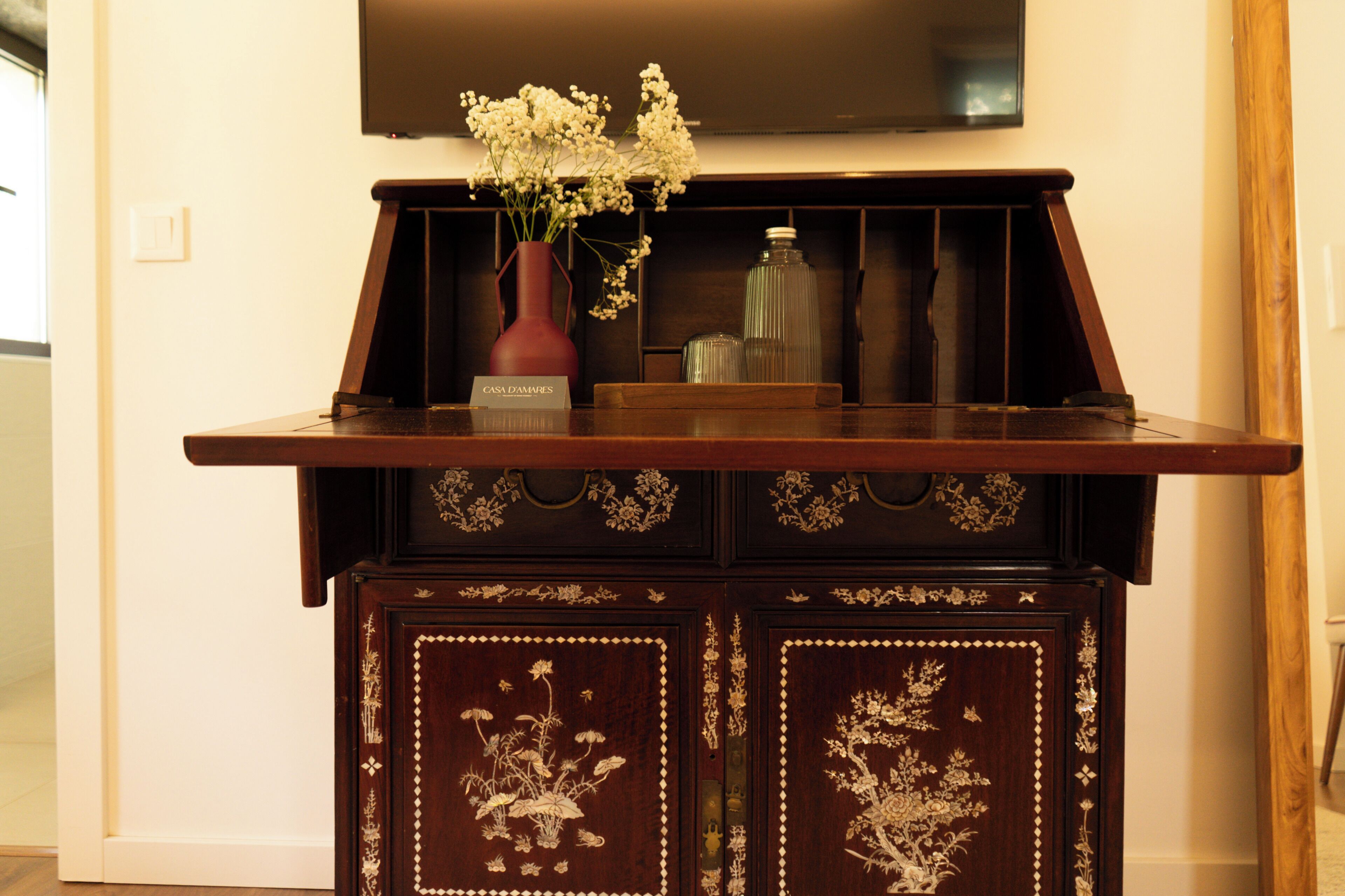 A wooden cabinet with intricate floral carvings and a vase with flowers on top.