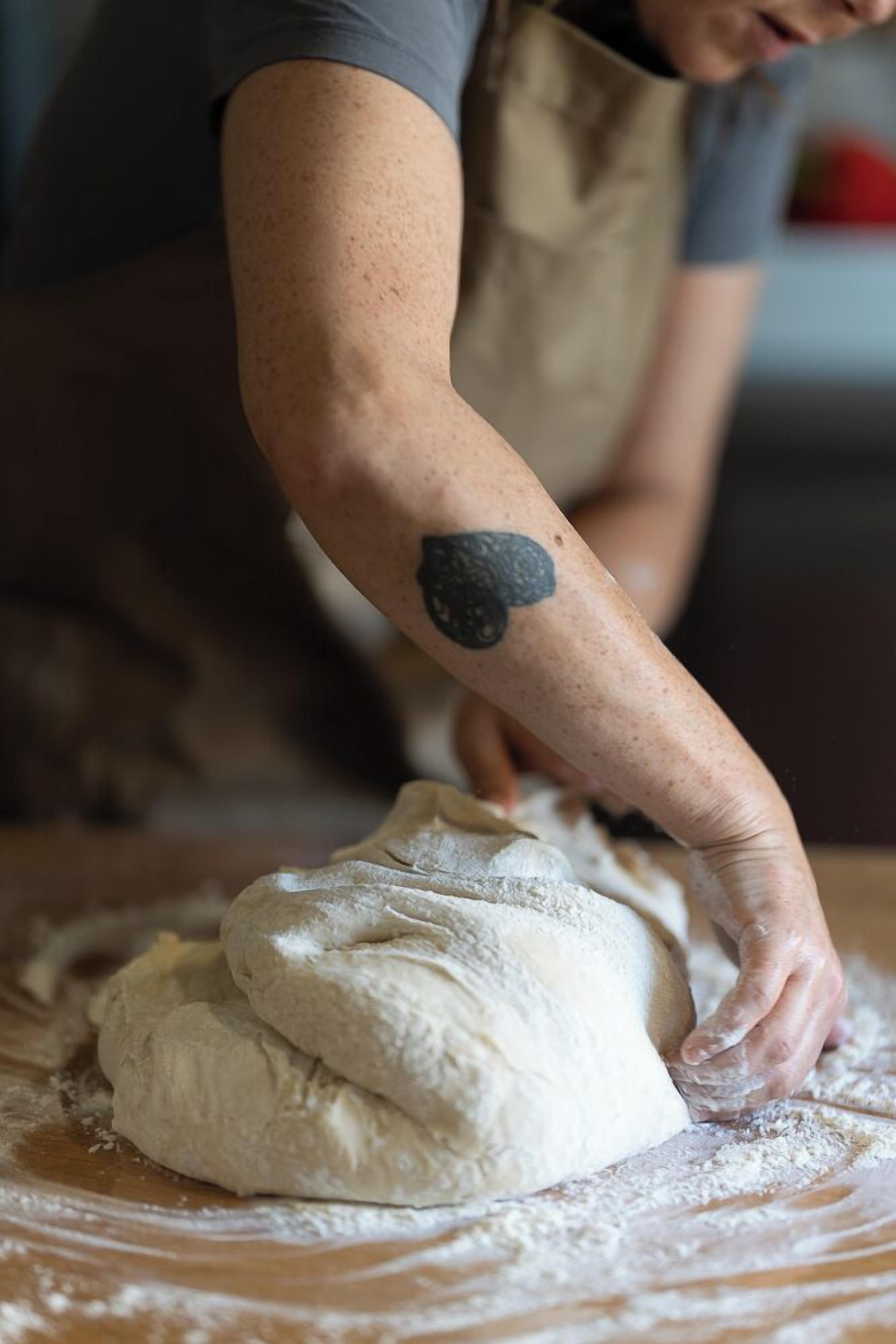A person kneading dough on a wooden surface with flour scattered around.