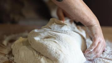 A person kneading dough on a wooden surface with flour scattered around.