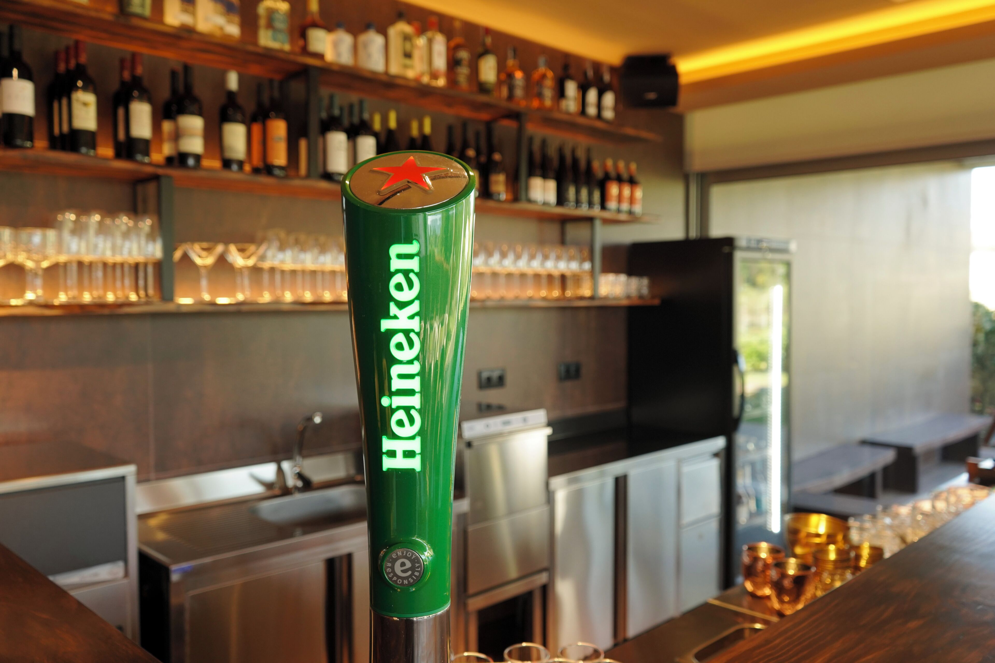 Baaritiski, jossa on Heineken-oluthana, hyllyjä pulloille ja lasiteline.