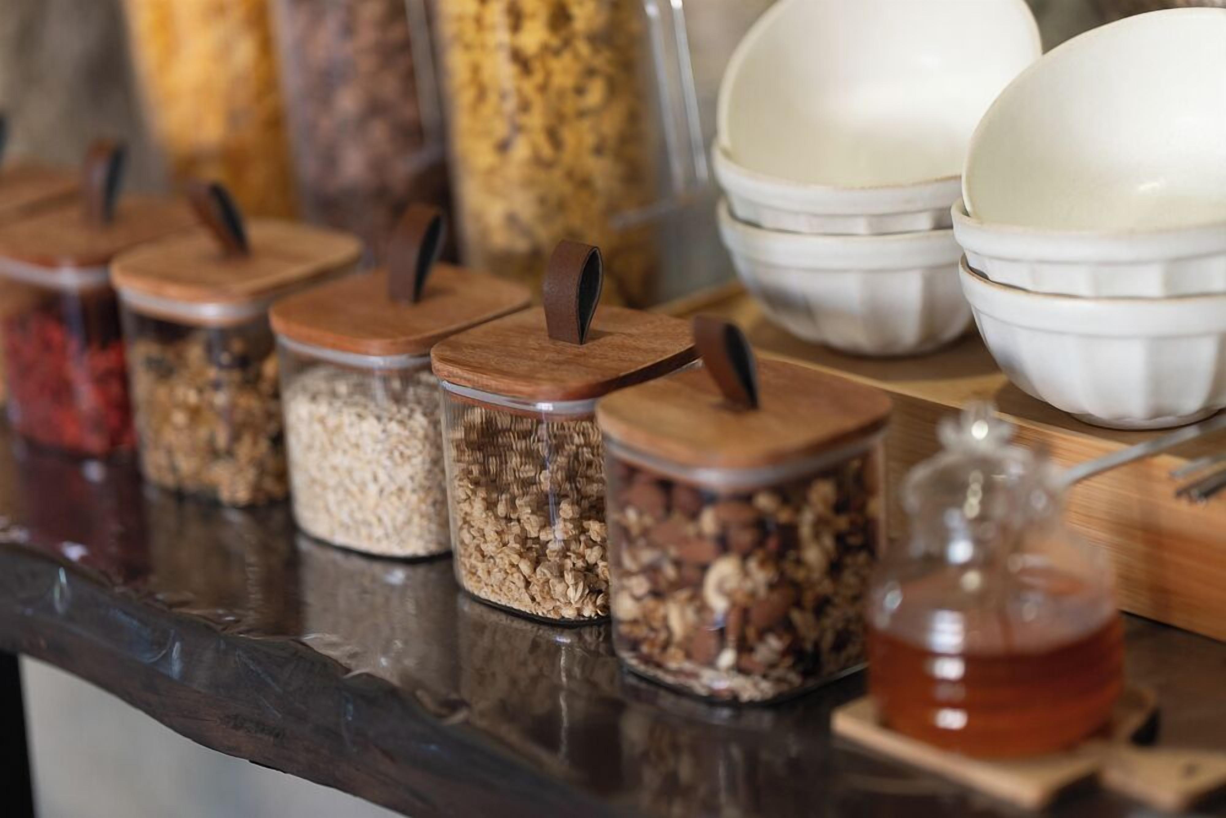 A kitchen counter with jars of granola and honey, and white bowls stacked in the background.