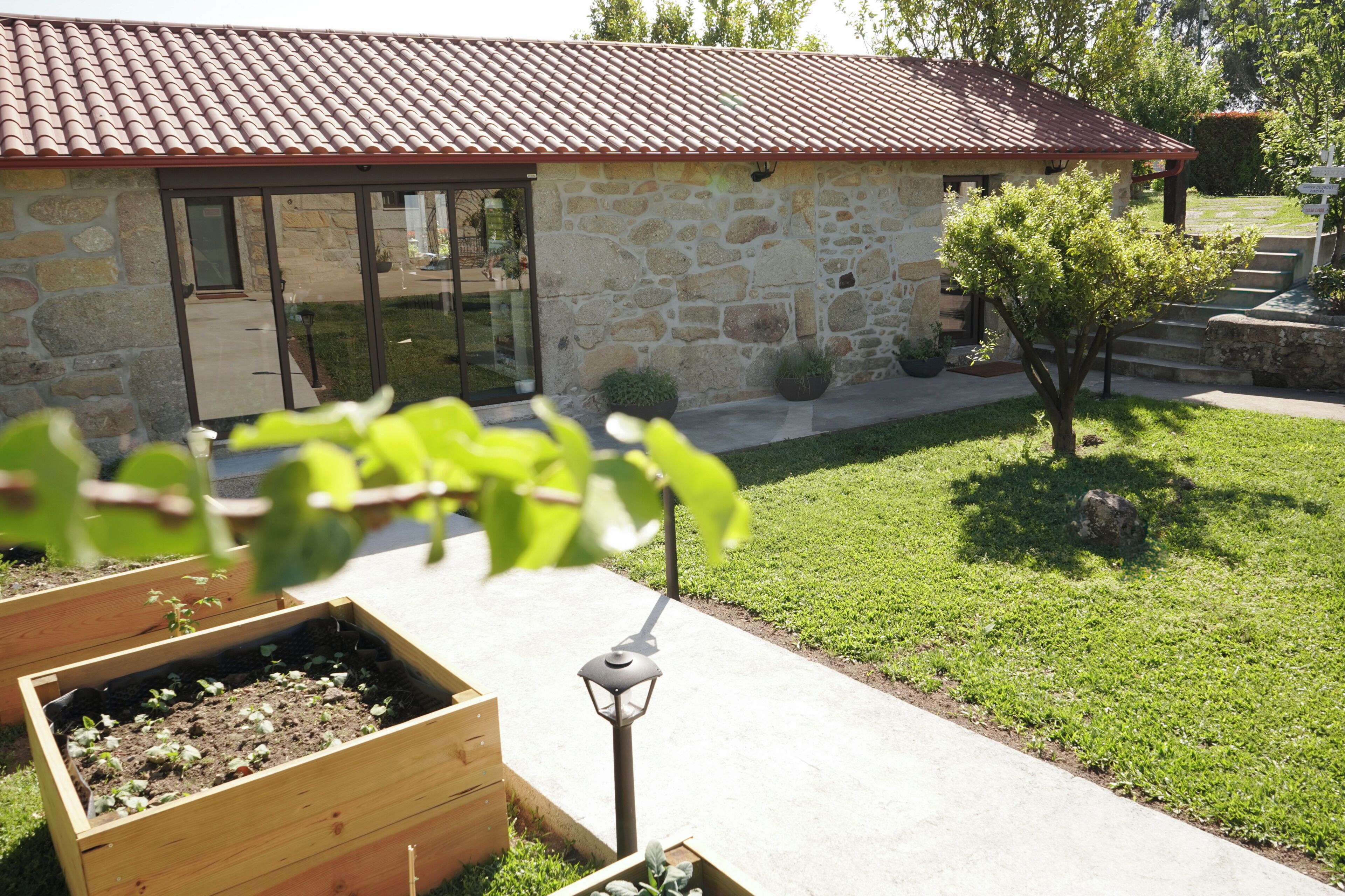 A stone building with a red-tiled roof, a wooden planter box, and a small tree.