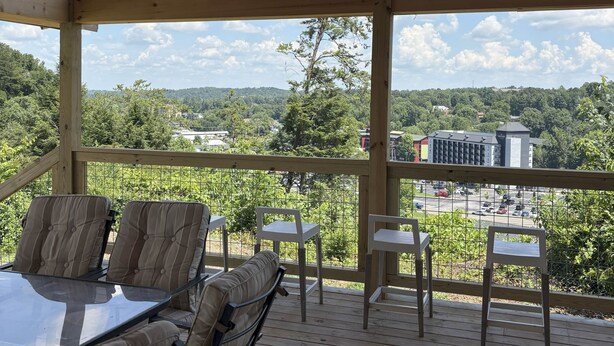 Una terraza al aire libre con una mesa y sillas, techo de madera y vista a un estacionamiento y edificios.