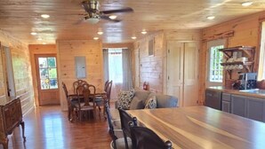Un comedor amplio con una mesa de madera larga y sillas, una zona de cocina con armarios y electrodomésticos, y un ventilador de techo.