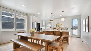A spacious kitchen with white cabinets, a wooden dining table with benches, and pendant lighting. - Modern 6br near skiing, luxe, sleeps 12, hot tub (Heber City)