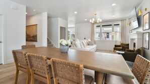 A spacious dining area with a long wooden table and woven chairs, a cozy living room with a sofa and armchairs, and a fireplace. - Modern 6br near skiing, luxe, sleeps 12, hot tub (Heber City)