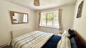 Un dormitorio con cama, ventana con cortinas, radiador y lámpara colgante.