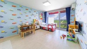 Ein Kinderzimmer mit Spielbereich, einem Bett, einem Schreibtisch und Blick ins Freie.