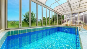 A swimming pool with a view of a green landscape through large windows. - Suncheon The Sky Pool Villa (Suncheon)