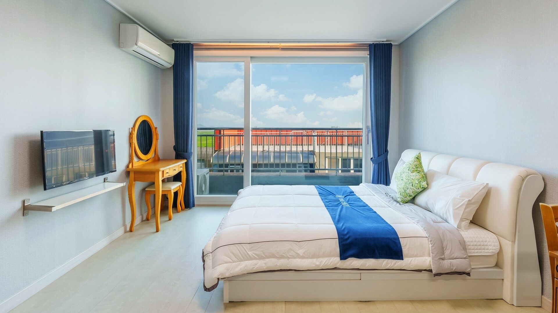 A modern hotel room with a bed, a desk, a chair, a TV, and a large window with a view of a bridge.