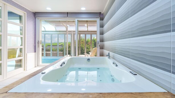 Un baño moderno con una bañera grande, una puerta de cristal que da a un balcón y vistas a un jardín.