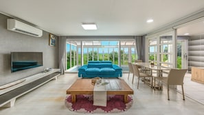 A modern living room with a flat-screen TV, a blue sofa, a wooden coffee table, and a dining area with a table and chairs. - Suncheon The Sky Pool Villa (Suncheon)