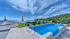 Una piscina con solárium de piedra, sillones de descanso y vistas al mar y a las montañas.