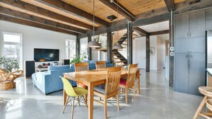 Un vaste espace de vie comprenant une table à manger en bois, un canapé bleu et un escalier menant à un autre niveau.
