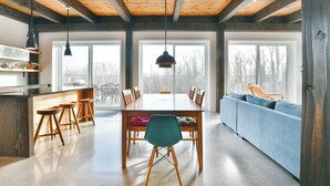 Un vaste espace dédié à la salle à manger, avec une table et des chaises en bois, un canapé bleu et de grandes fenêtres offrant une vue sur l’extérieur.