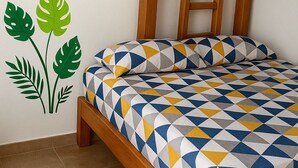En säng med en enkel sänggavel, ett sängöverkast med geometriskt mönster och en väggdekor i form av gröna löv.