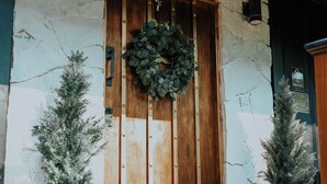 A rustic stone building with a wooden door, two potted plants, and a wreath.