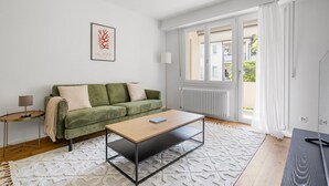 Uma sala de estar moderna com um sofá verde, uma mesa de centro de madeira e uma janela grande com cortinas brancas.