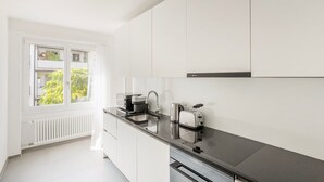 Cozinha moderna com armários brancos, bancada preta, forno embutido e janela com vista para o verde.
