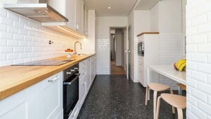 Cuina moderna amb armaris blancs, taulell de fusta i un frontissó de rajoles negres.