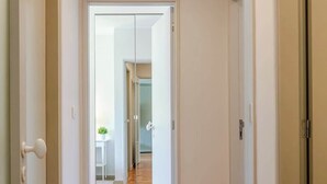 Passadís amb sòl de fusta i parets blanques, que condueix a una habitació amb miralls i una cuina a la vista.